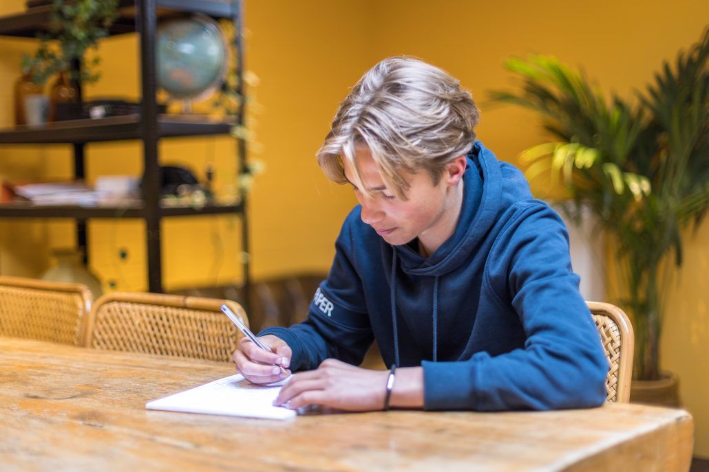 Scholier werkt geconcentreerd aan huiswerk bij mooi jong in Den Haag